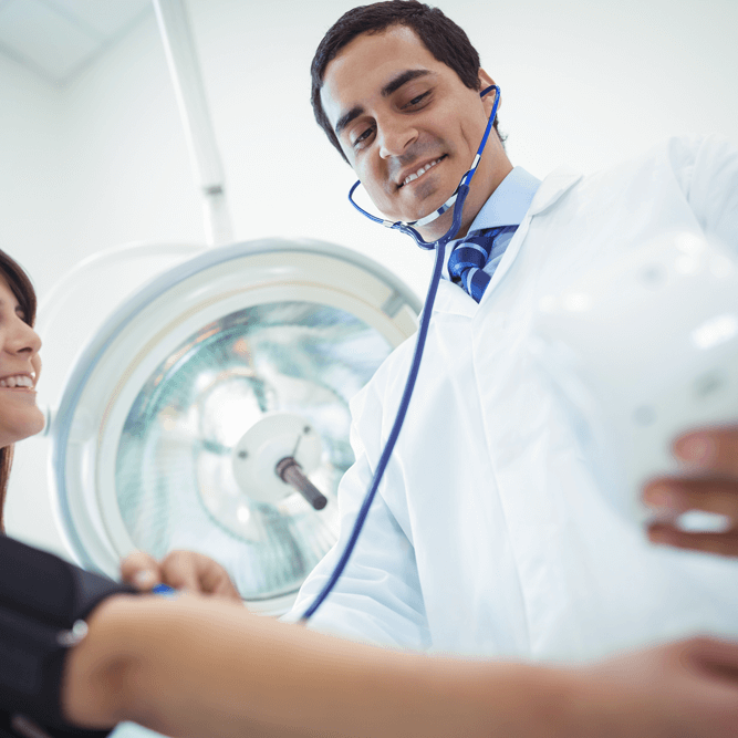 doctor-checking-female-patient-blood-pressure-2025-04-03-09-30-54-utc A doctor in a white coat takes measurements with medical equipment while a patient sits, preparing for examination in a clinical setting.