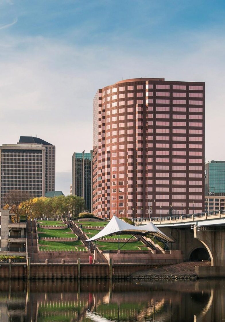 hartford 2 Panoramic view of Hartford, Connecticut, featuring modern buildings, a bridge, and a park along the river under a clear sky.