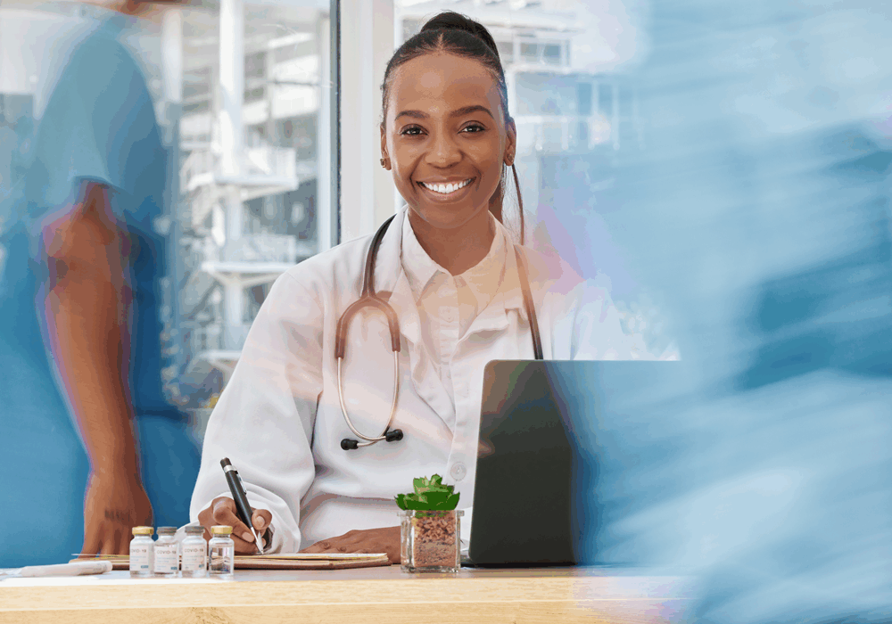 portrait-black-woman-and-doctor-writing-in-hospit-2025-04-06-10-16-09-utc-(1) A doctor in a white coat and stethoscope sits at a desk with a laptop, writing notes beside a small potted plant and vials.
